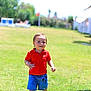 child, toddler, smiling, red_shirt, blue_shorts, mickey_mouse, grass, lawn, sunny, outdoors, park, daylight, play, baby_hands, face, portrait, vacation, resort, sunlounger, bright