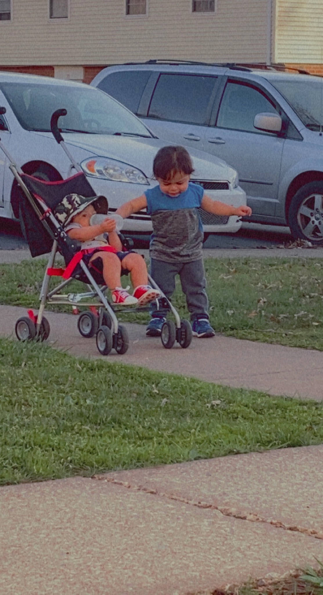 William is registered to the contest to win money with this photo: asphalt, automotive_exterior, automotive_tire, automotive_wheel_system, baby_carriage, car, grass, land_vehicle, lawn, motor_vehicle, parking, person, plant, recreation, rolling, shorts, tire, toddler, vehicle, vehicle_door