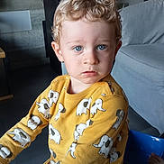 Manoé a rejoint le concours — aidez-le/la à gagner de superbes lots ! child, toddler, curly_hair, blue_eyes, yellow_shirt, elephant_print, indoor, sofa, furniture, person, portrait, casual_clothing, cute, young_child, seated, floor, light, expression, modern_interior, curiosity