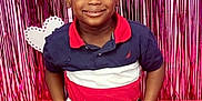 Akheem is registered to the contest to win money with this photo: child, boy, smiling, sitting, red, pink, heart, backdrop, party, celebration, happy, casual_clothing, indoor, portrait, cute, young, person, colorful, decor, fun