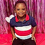 child, boy, smiling, sitting, red, pink, heart, backdrop, party, celebration, happy, casual_clothing, indoor, portrait, cute, young, person, colorful, decor, fun
