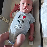 Jax Cane Prater is registered to the contest to win money with this photo: baby, infant, onesie, clothing, crib, bassinet, face, person, child, newborn, cute, lying_down, hand, foot, expression, indoor, fabric, text_on_clothing, love, parental_affection