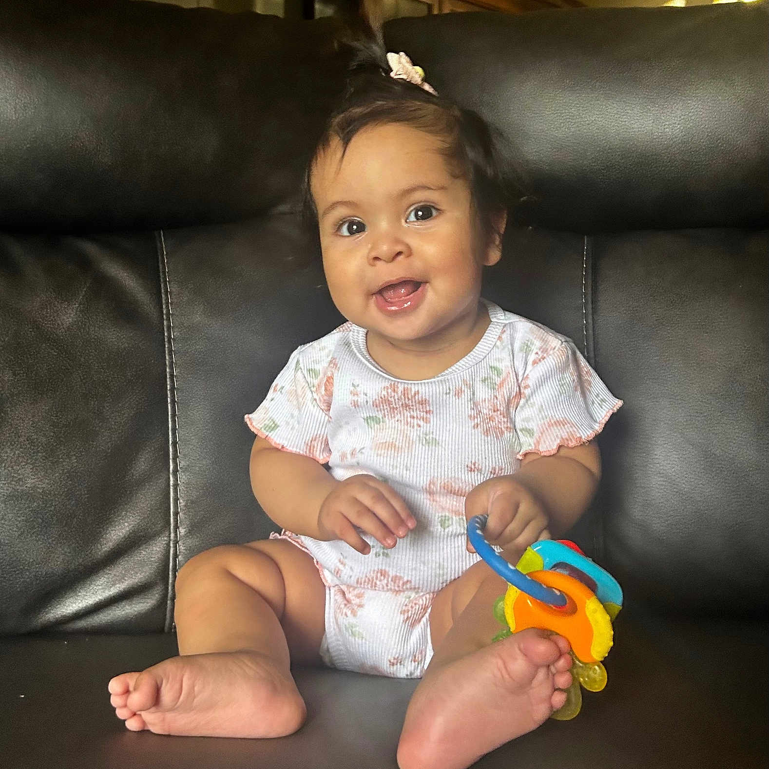 Yessiah Michelle joined the competition — help win amazing prizes! baby, child, smiling, toy, onesie, hair_clip, sitting, leather_couch, indoor, happy, cute, infant, portrait, playful, foot, hand, person, young_child, domestic, bright