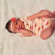 Priscilla joined the competition — help win amazing prizes! baby, infant, onesie, headband, flower, watermelon_print, blanket, soft_texture, lying_down, cute, pink_clothing, newborn, hand_near_mouth, curious_look, skin, small_feet, indoors, portrait, child, adorable