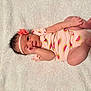 baby, infant, onesie, headband, flower, watermelon_print, blanket, soft_texture, lying_down, cute, pink_clothing, newborn, hand_near_mouth, curious_look, skin, small_feet, indoors, portrait, child, adorable