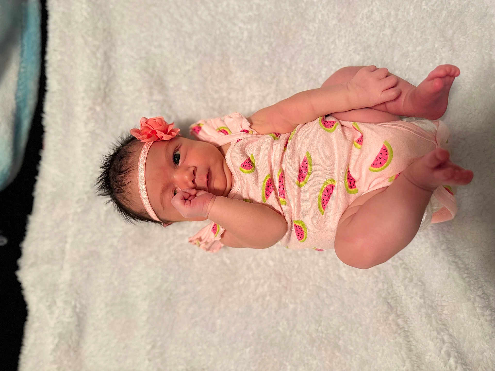 Priscilla joined the competition — help win amazing prizes! baby, infant, onesie, headband, flower, watermelon_print, blanket, soft_texture, lying_down, cute, pink_clothing, newborn, hand_near_mouth, curious_look, skin, small_feet, indoors, portrait, child, adorable