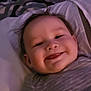 baby, child, smiling, tongue_out, striped_shirt, bed, blanket, pattern, indoor, face, happy, infant, person, cute, portrait, young_child, lying_down, cozy, soft_light, closeup
