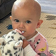 Charlotte joined the competition — help win amazing prizes! baby, child, plush_toy, cow, pajamas, floor, indoor, carpet, cute, young_child, person, face, hand, sitting, toy, animal_pattern, home, infant, portrait, chewing