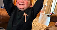 Cain is registered to the contest to win money with this photo: toddler, child, happy, smiling, raising_hands, black_sweatshirt, cross_symbol, jeans, indoor, living_room, carpet, couch, curtains, wood_floor, cabinet, refrigerator, warm_lighting, person, home, cheerful