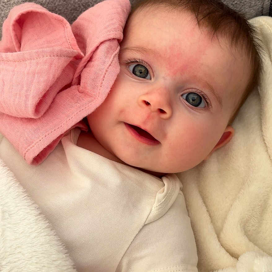 Alba participe au concours pour gagner de l'argent avec cette photo : baby, infant, face, eyes, blanket, clothing, pink_cloth, lying_down, soft_texture, cute, skin, head, expression, indoors, portrait, child, newborn, cozy, sleepwear, comfort