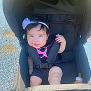 Violet joined the competition — help win amazing prizes! baby, stroller, child, smiling, headband, flower, baby_bottle, black_clothing, outdoor, sunlight, happy, infant, seatbelt, baby_girl, person, cute, portrait, baby_face, sitting, playground_surface