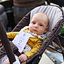 baby, stroller, infant, child, portrait, face, blue_eyes, beads, clothing, yellow_shirt, outdoor, plant, flower, card, sitting, cute, young_child, relaxed, person, closeup