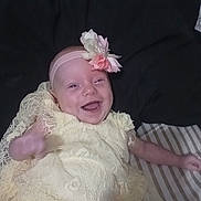Lilyann joined the competition — help win amazing prizes! apparel, baby, blanket, child, cute, dress, flower, hand, happy, head, headband, indoors, infant, lace, lying_down, person, portrait, skin, smile, striped_surface