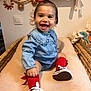 baby, child, smile, red_bow, red_socks, blue_shirt, sneakers, indoor, changing_pad, wicker_basket, happy, cute, toy, knitted_toy, decor, person, face, sitting, toddler, infant