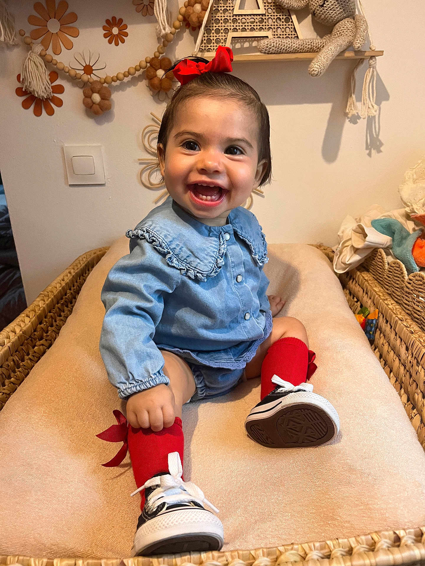 Ava participe au concours pour gagner de l'argent avec cette photo : baby, child, smile, red_bow, red_socks, blue_shirt, sneakers, indoor, changing_pad, wicker_basket, happy, cute, toy, knitted_toy, decor, person, face, sitting, toddler, infant