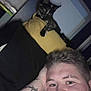 Buddie joined the competition — help win amazing prizes! selfie, person, cat, tortoiseshell_cat, pillow, tattoo, barbed_wire_tattoo, bedroom, indoors, dim_lighting, curious_cat, face, head, hand, resting, black_pillow, yellow_pillow, wall, relaxed, nighttime