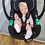baby, infant, car_seat, black, pink_clothing, polka_dot_socks, blue_eyes, carrying_handle, flooring, carpet, wood_floor, safety_harness, child, indoor, cute, small, seated, baby_gear, portrait, childcare
