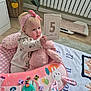 baby, baby_clothes, baby_mat, child, cushion, cute, floor_rug, home, indoor, infant, milestone_card, pink_bunny, pink_headband, plant, play_area, portrait, radiator, sitting, soft_toy, wooden_floor