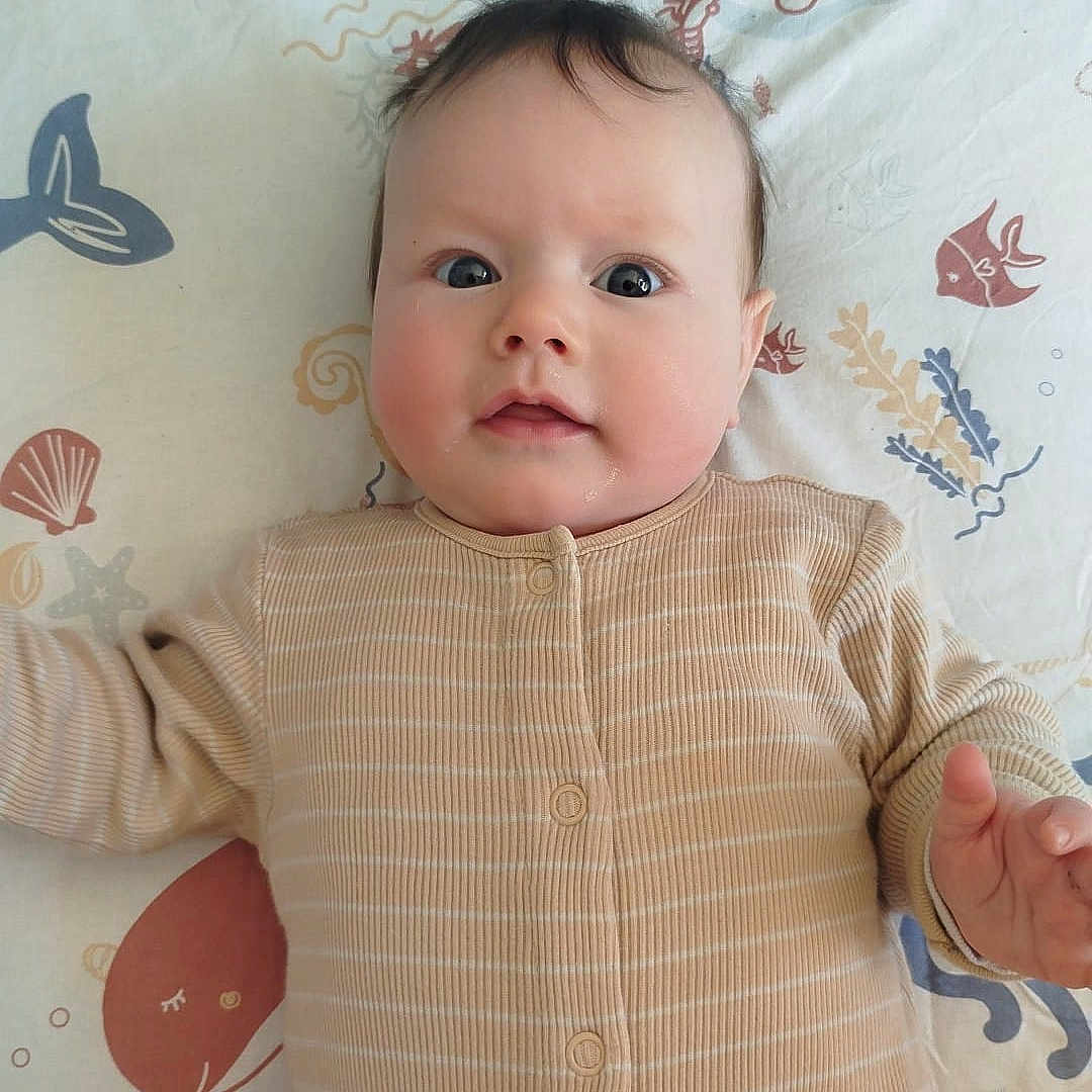 Anya a rejoint le concours — aidez-le/la à gagner de superbes lots ! baby, infant, onesie, blanket, sea_theme, fish_pattern, shell_pattern, face, drool, curious, lying_down, child, cute, soft_lighting, indoor, portrait, young_child, head, hands, close_up