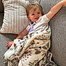 blanket, casual_clothing, child, comfortable, couch, cozy, face, hair, happy, home, indoor, kid, patterned_blanket, pillow, portrait, relaxing, resting, smile, striped_pillow, young_child