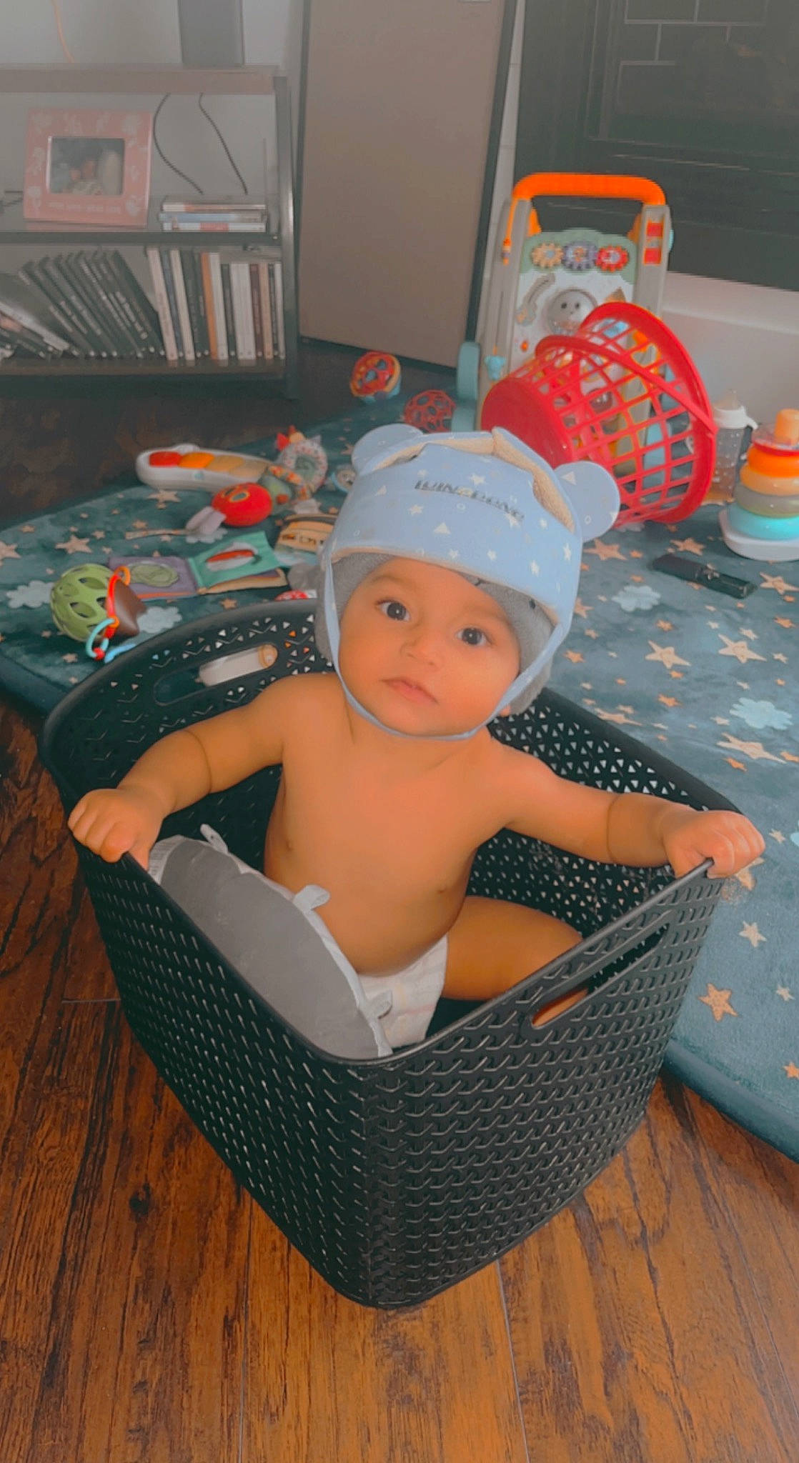 Ezra is registered to the contest to win money with this photo: baby, baby_products, baby_toddler_clothing, bathing, cap, child, comfort, fashion_accessory, flooring, fun, hardwood, headwear, laundry_basket, leisure, person, personal_protective_equipment, play, room, sitting, toddler