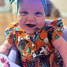 Zonasue is registered to the contest to win money with this photo: baby, child, smiling, headband, colorful_clothing, high_chair, indoor, portrait, happy, infant, person, cute, closeup, sitting, apparel, patterned_shirt, home, young_child, face, cheerful