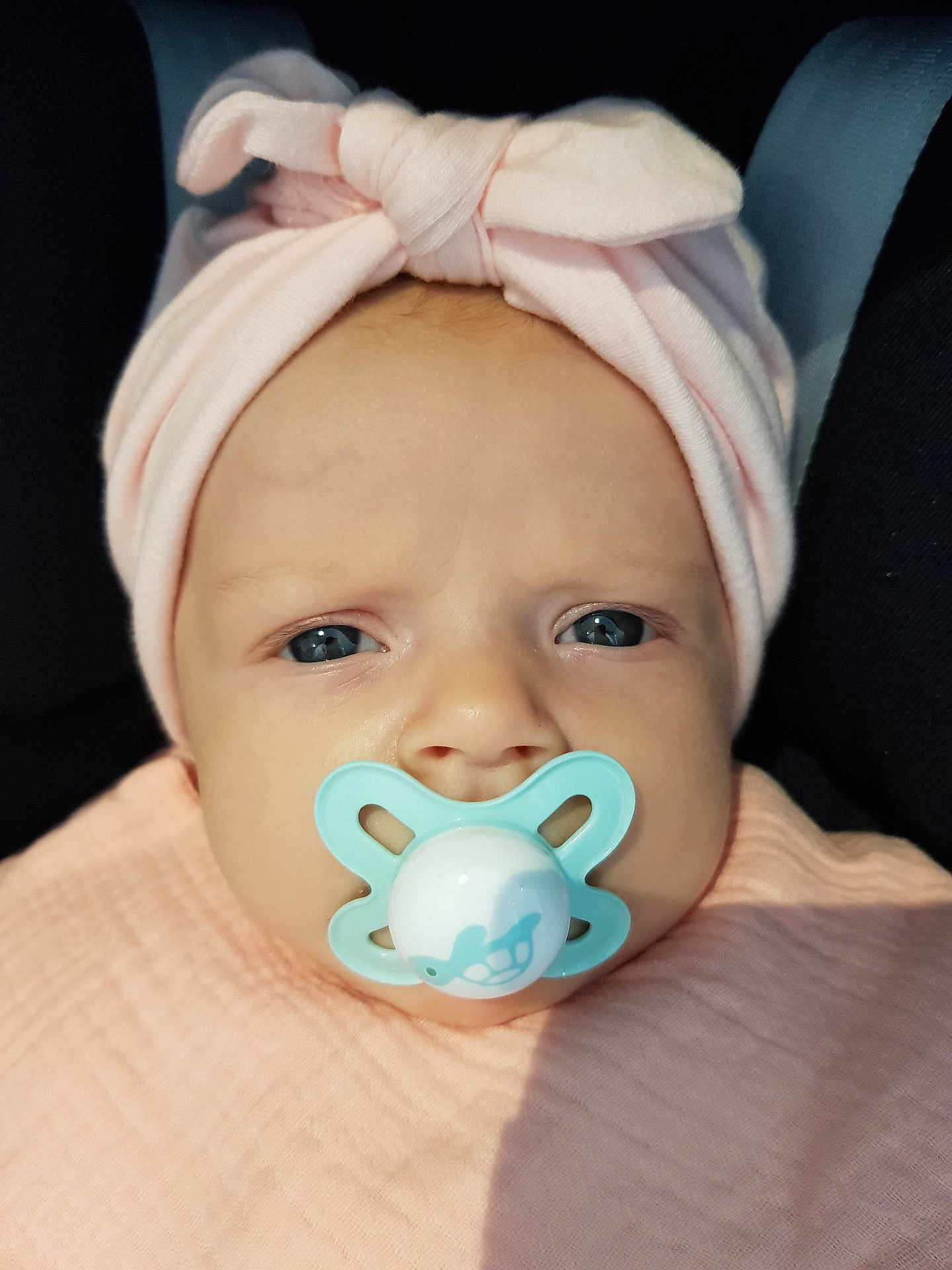 Léonie participe au concours pour gagner de l'argent avec cette photo : baby, pacifier, headwrap, pink, blue_eyes, close_up, infant, blanket, cute, face, child, newborn, soft_light, portrait, indoors, expression, wrapped, wearing, headwear, skin