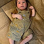 Chance is registered to the contest to win money with this photo: baby, infant, couch, overalls, brown_shirt, soft_furniture, patterned_clothing, indoor, carpet, cute, child, person, relaxed, skin, foot, hand, expression, seated, looking_at_camera, young
