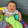 baby, smiling, child, blanket, toys, cushion, colorful, striped_clothing, grass, brick_wall, happy, infant, playtime, indoors, comfort, person, cute, small_child, sitting, fabric