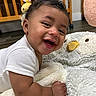 baby, smiling, drool, white_onesie, crib, nursery, toy, stuffed_animal, owl_blanket, wooden_furniture, floor, happy, infant, child, cute, indoors, soft_texture, playtime, portrait, person