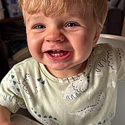 Isaac a rejoint le concours — aidez-le/la à gagner de superbes lots ! toddler, child, smiling, high_chair, indoor, blonde_hair, dinosaur_print, shirt, happy, cute, face, teeth, portrait, young_child, baby, person, casual_clothing, home, furniture, expression