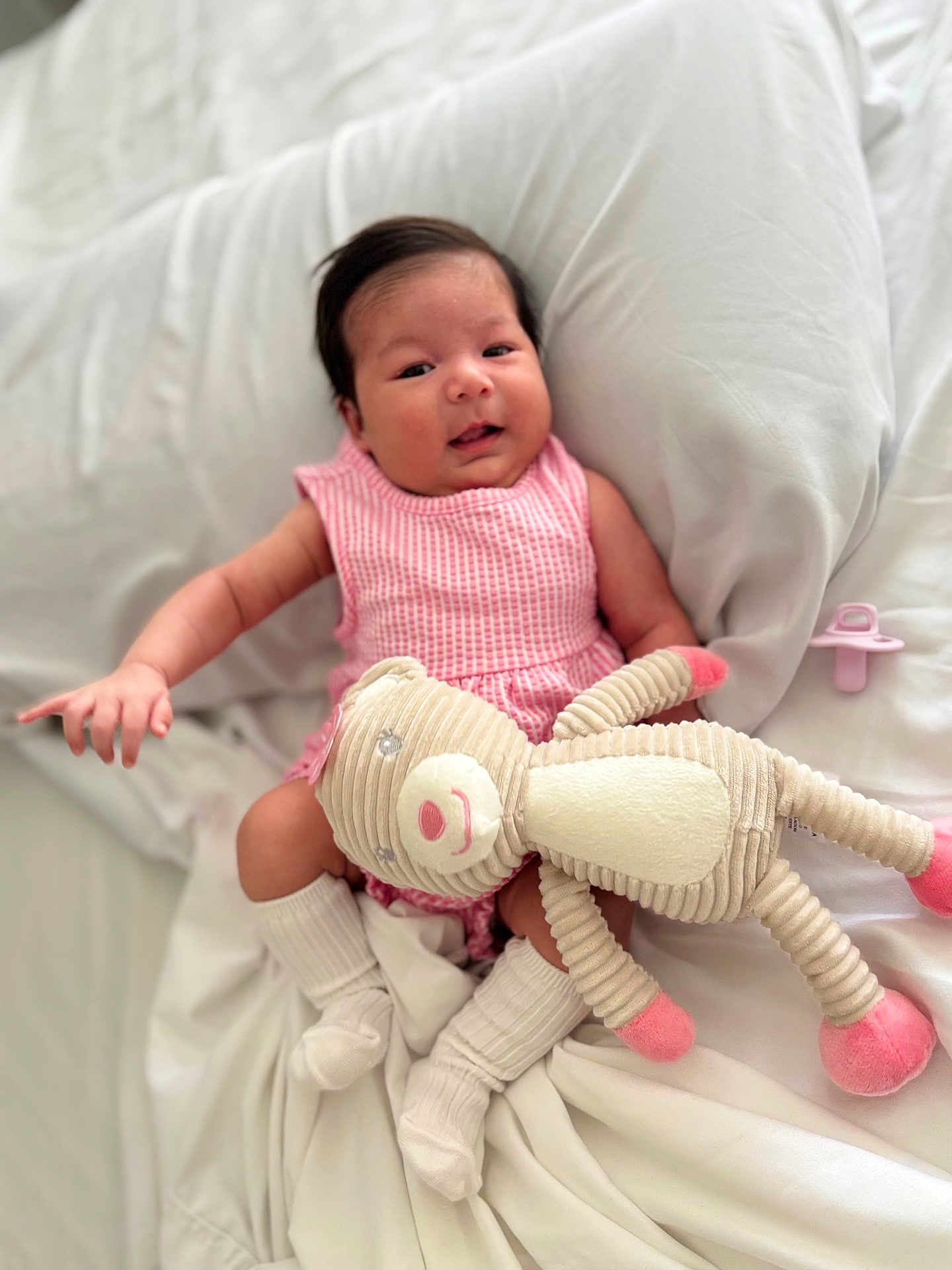 Lariany is registered to the contest to win money with this photo: baby, infant, pink_dress, stuffed_animal, pacifier, white_bed, blanket, socks, cute, smiling, indoors, soft_toy, baby_girl, resting, cozy, child, portrait, comfort, sleepwear, happy