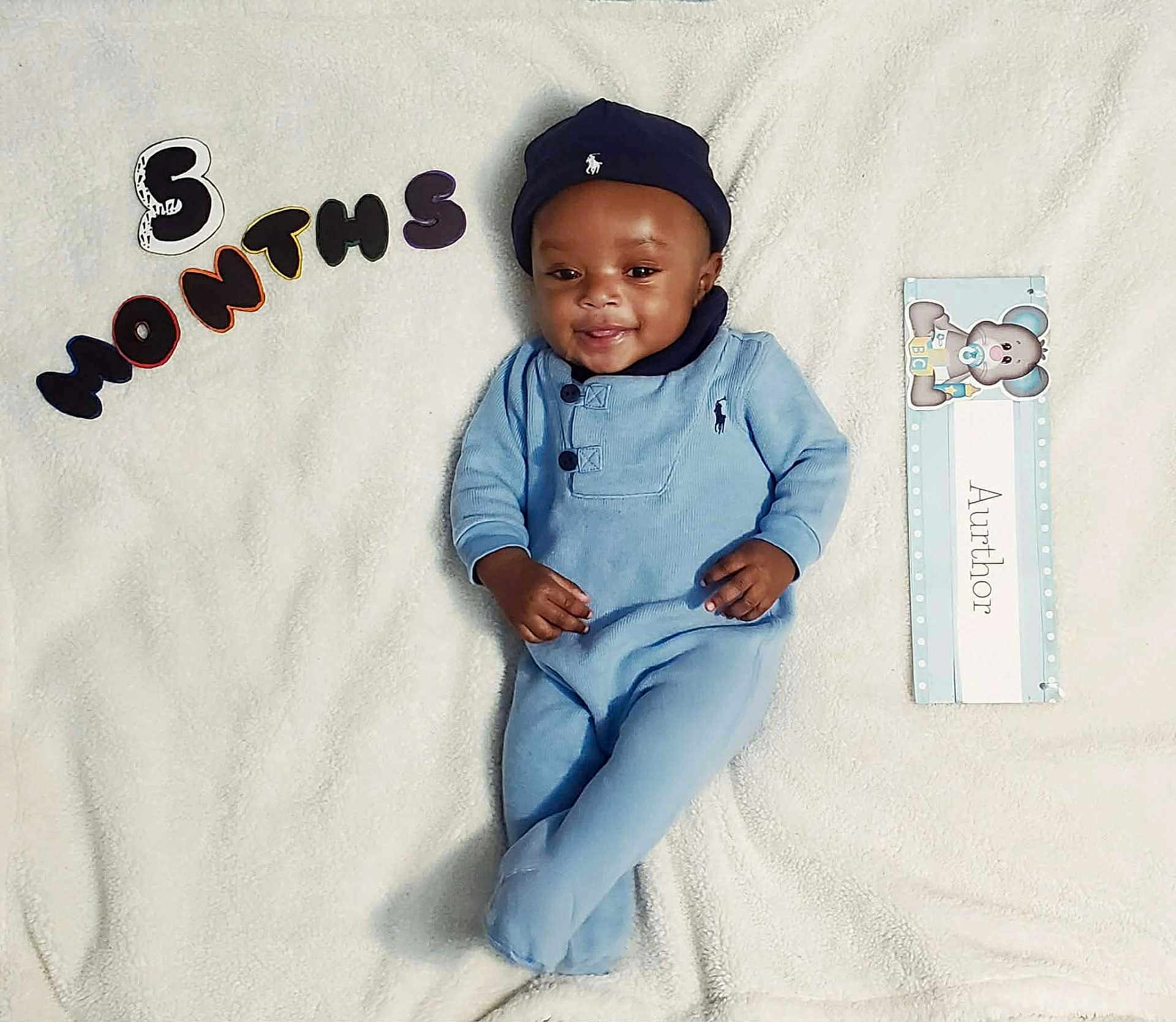 Aurthor is registered to the contest to win money with this photo: baby, infant, smiling, blue_clothing, hat, blanket, milestone, 5_months, lying_down, cute, indoors, portrait, child, soft_texture, name_card, teddy_bear, happy, young, cozy, baby_photo