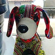 Nounours participe au concours pour gagner de l'argent avec cette photo : stuffed_animal, dog, toy, fabric, patterned, colorful, window, windowsill, indoor, decorative, black_nose, black_eyes, red, green, yellow, embroidered, soft_toy, animal_figure, background, roof