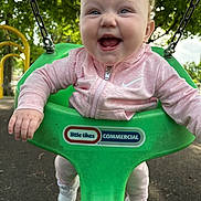 Josephine Elizabeth is registered to the contest to win money with this photo: baby, child, swing, playground, green_swing, pink_hoodie, happy, smiling, outdoor, trees, park, daylight, play, joy, infant, clothing, footwear, chain, person, fun