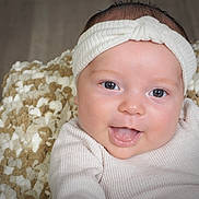 Lily joined the competition — help win amazing prizes! baby, infant, face, headband, tongue_out, blue_eyes, blanket, close_up, smiling, cute, child, soft_texture, white_clothing, happy, portrait, indoor, skin, newborn, person, expression