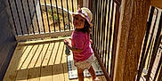 Ariana Michelle joined the competition — help win amazing prizes! balcony, child, curious, daylight, hat, nature, outdoor, pink_shirt, portrait, railing, sandal, shadow, shorts, small_object, standing, summer_clothing, sunlight, toddler, trees, wood_floor