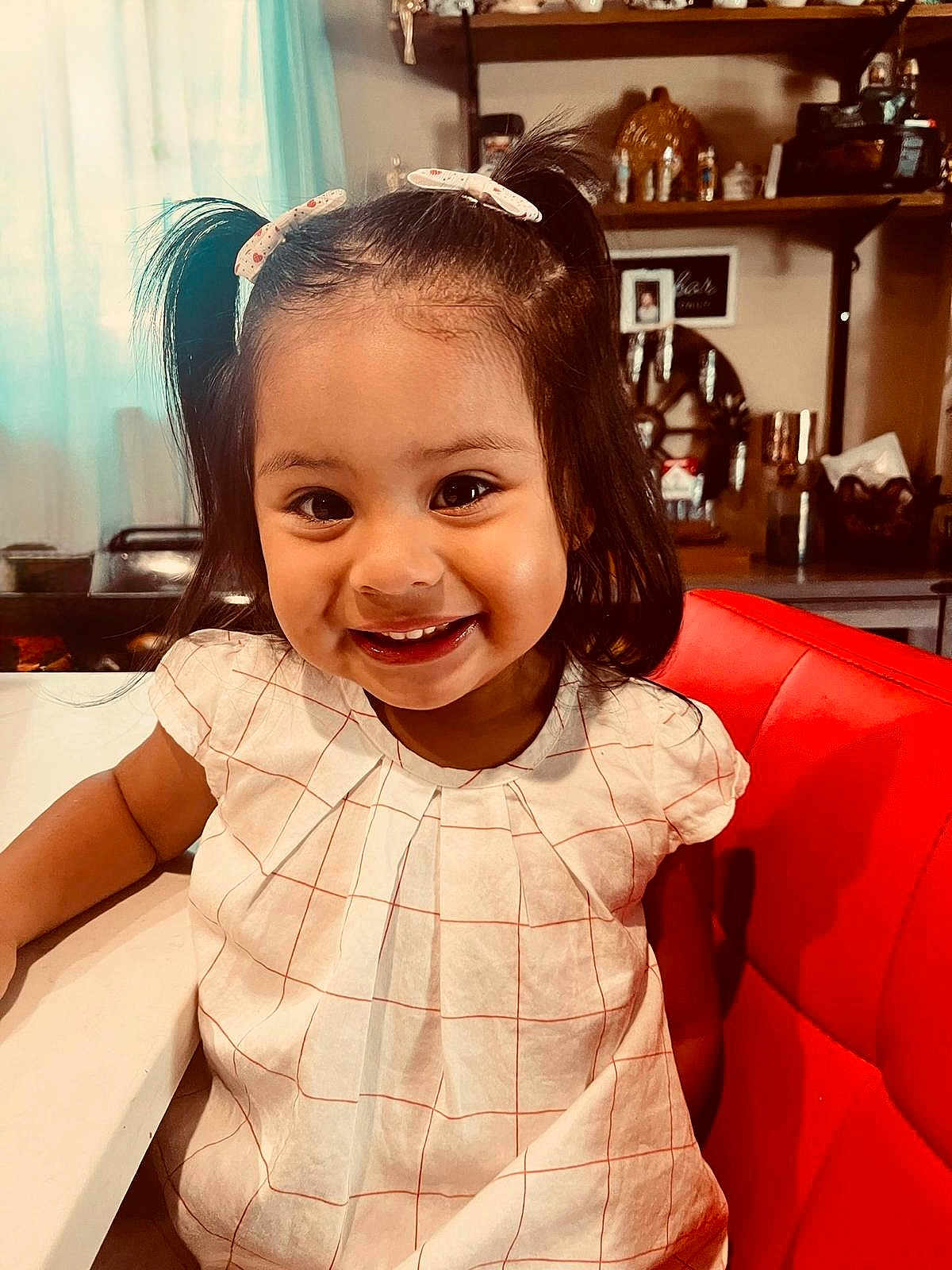 Ariana Michelle is registered to the contest to win money with this photo: child, girl, smile, pigtails, hair_clips, red_chair, white_table, indoor, cute, happy, portrait, clothing, furniture, person, face, young_child, dressed, home, decor, cheerful