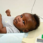 Elya-Victoria participe au concours pour gagner de l'argent avec cette photo : baby, infant, medical_scale, lying_down, gray_shirt, curly_hair, earrings, blue_paper, looking_at_camera, indoors, health_check, skin, child, person, portrait, cute, young, measurement, expression, resting