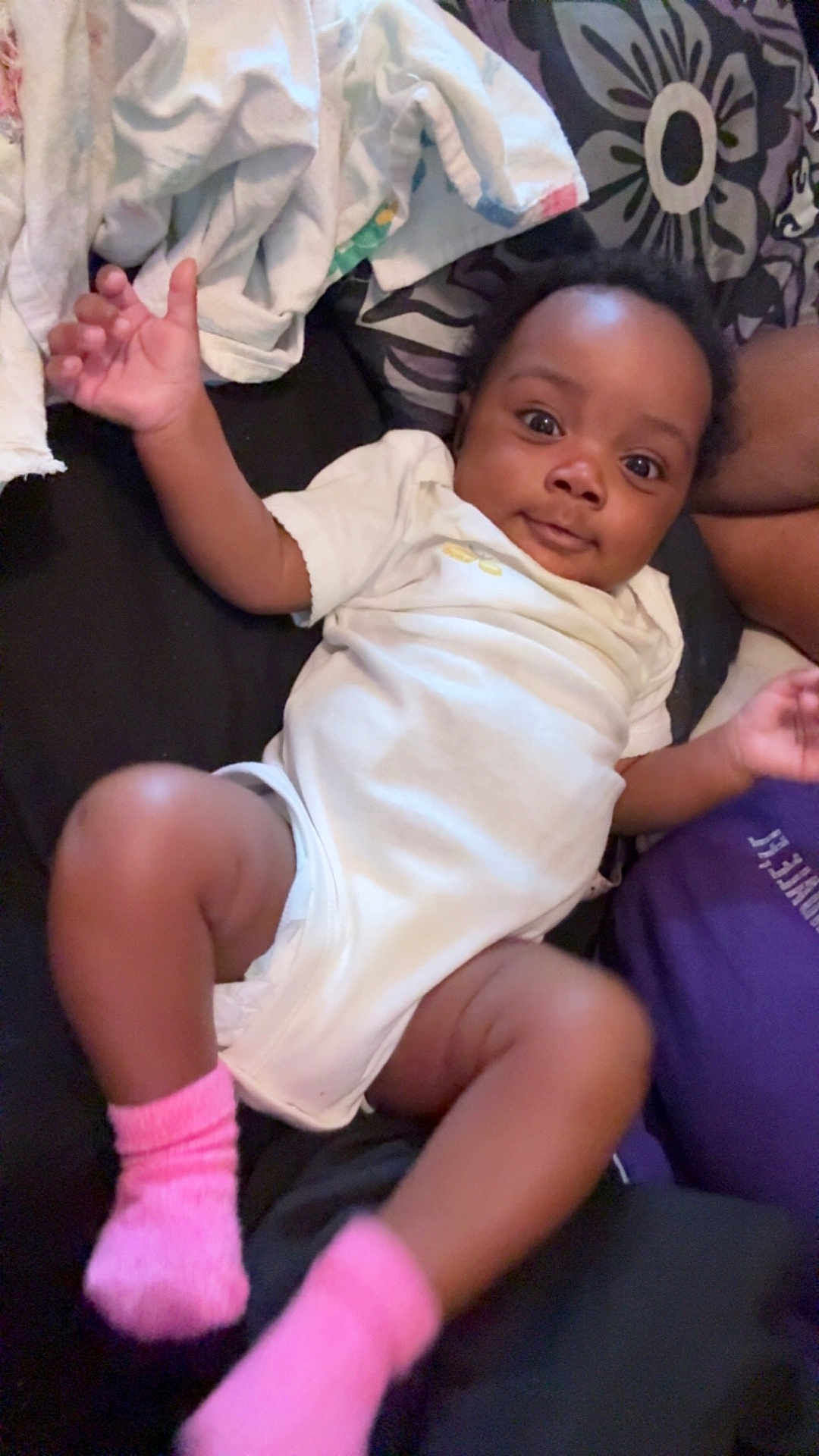 Kyleigh is registered to the contest to win money with this photo: baby, infant, child, onesie, pink_socks, smiling, lying_down, blanket, cushion, indoor, person, cute, happy, skin, face, hand, foot, black_hair, expression, clothing