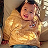 child, toddler, smiling, portrait, seated, indoors, chair, sweater, fleece, yellow, deer, hair_bow, dark_hair, sunlight, window_shadows, casual_clothing, blue_jeans, happy, cute, photography