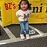 Shakira joined the competition — help win amazing prizes! child, girl, toddler, portrait, smiling, standing, outdoor, parking_lot, yellow_background, shop, banner, sweater, minnie_mouse, jeans, sneakers, long_hair, dark_hair, fashion, full_body, happy