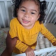 Leeah joined the competition — help win amazing prizes! toddler, child, smiling, yellow_shirt, crib, hand, person, indoor, curly_hair, bed, toy, furniture, happy, holding, portrait, baby, cute, skin, face, cozy
