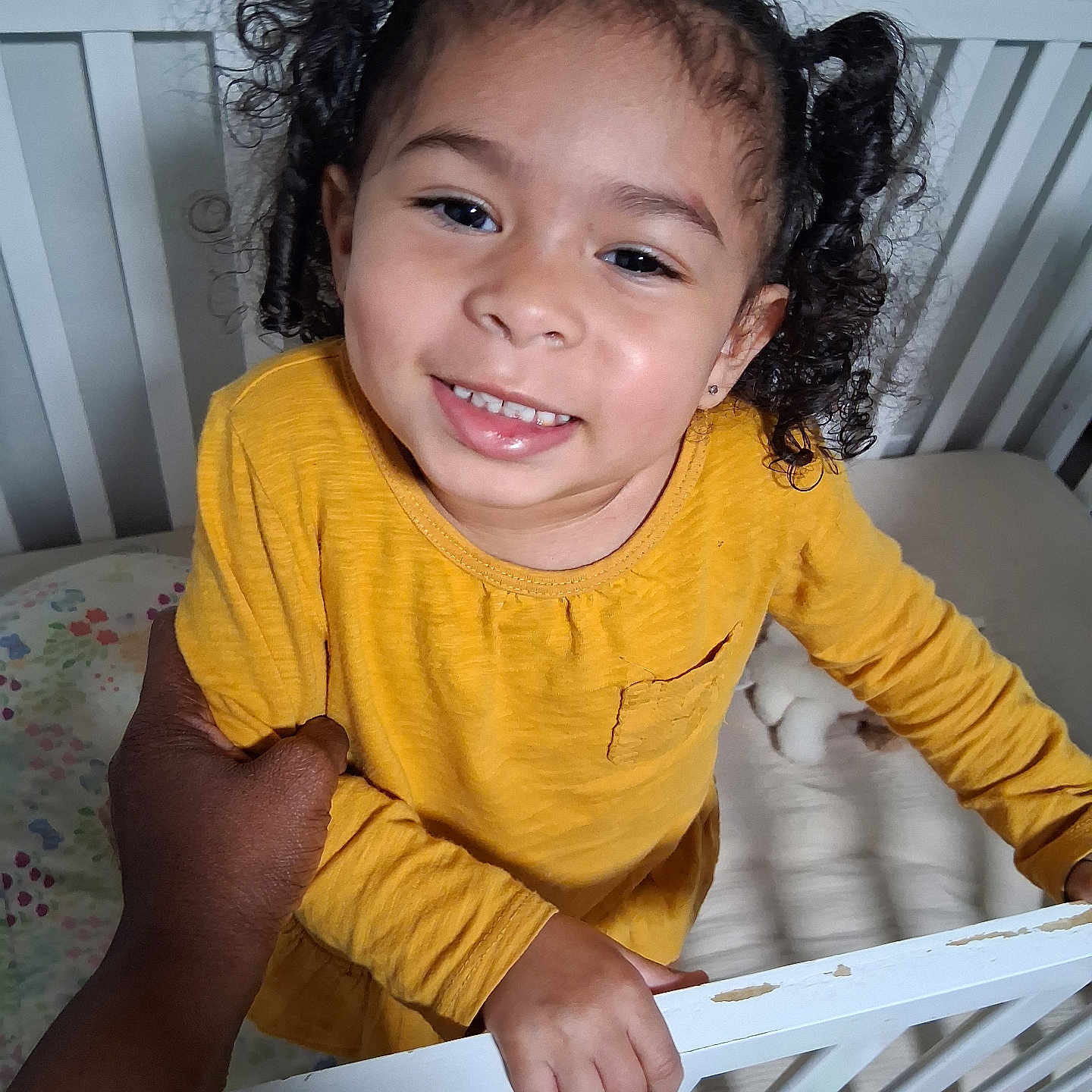 Leeah joined the competition — help win amazing prizes! baby, bed, child, cozy, crib, curly_hair, cute, face, furniture, hand, happy, holding, indoor, person, portrait, skin, smiling, toddler, toy, yellow_shirt