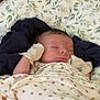 baby, newborn, sleeping, blanket, mittens, cushion, floral_pattern, striped, face, infant, cozy, resting, indoors, soft_lighting, peaceful, child, person, fabric, water_bottle, bedroom
