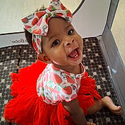 Saniyah joined the competition — help win amazing prizes! baby, bow, bright_colors, child, cute, face, happy, headband, indoors, infant, joyful, patterned_clothing, person, play, playpen, red, sitting, smile, tutu, young_child