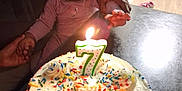 Saniyah is registered to the contest to win money with this photo: adult_hand, baby, birthday_cake, cake, candle, celebration, chair, child, cream, curious, face, flower, headband, holding_hands, indoor, light, person, pink_clothing, sprinkles, table