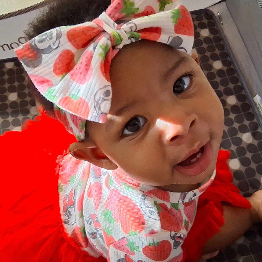 Saniyah is registered to the contest to win money with this photo: baby, bow, child, clothing, crawling, cute, eyes, face, hands, happy, headband, indoors, infant, patterned, person, playpen, red, smiling, strawberry_pattern, tutu