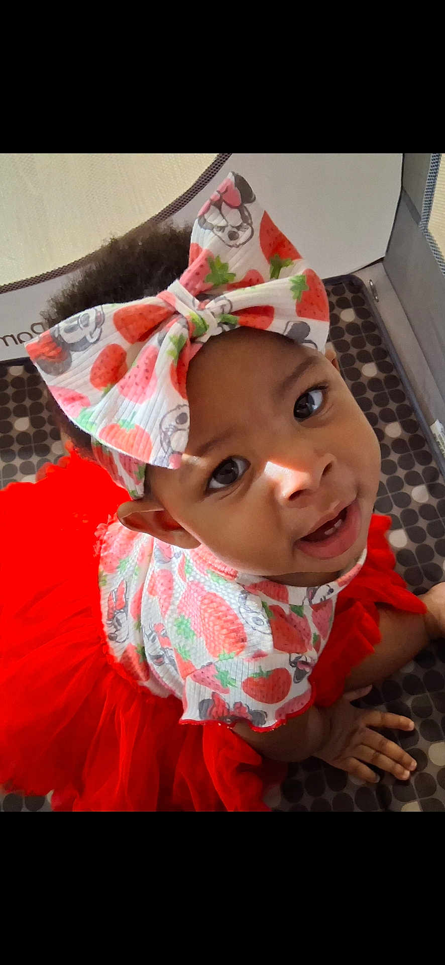 Saniyah is registered to the contest to win money with this photo: baby, child, tutu, headband, bow, strawberry_pattern, cute, smiling, playpen, infant, red, clothing, patterned, face, eyes, hands, crawling, indoors, happy, person