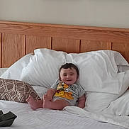 Maverick joined the competition — help win amazing prizes! baby, child, bed, pillow, smiling, indoors, wooden_headboard, white_bedspread, cartoon_shirt, feet, happy, person, portrait, relaxed, cushion, home_interior, wall_art, infant, sleeping_area, cozy